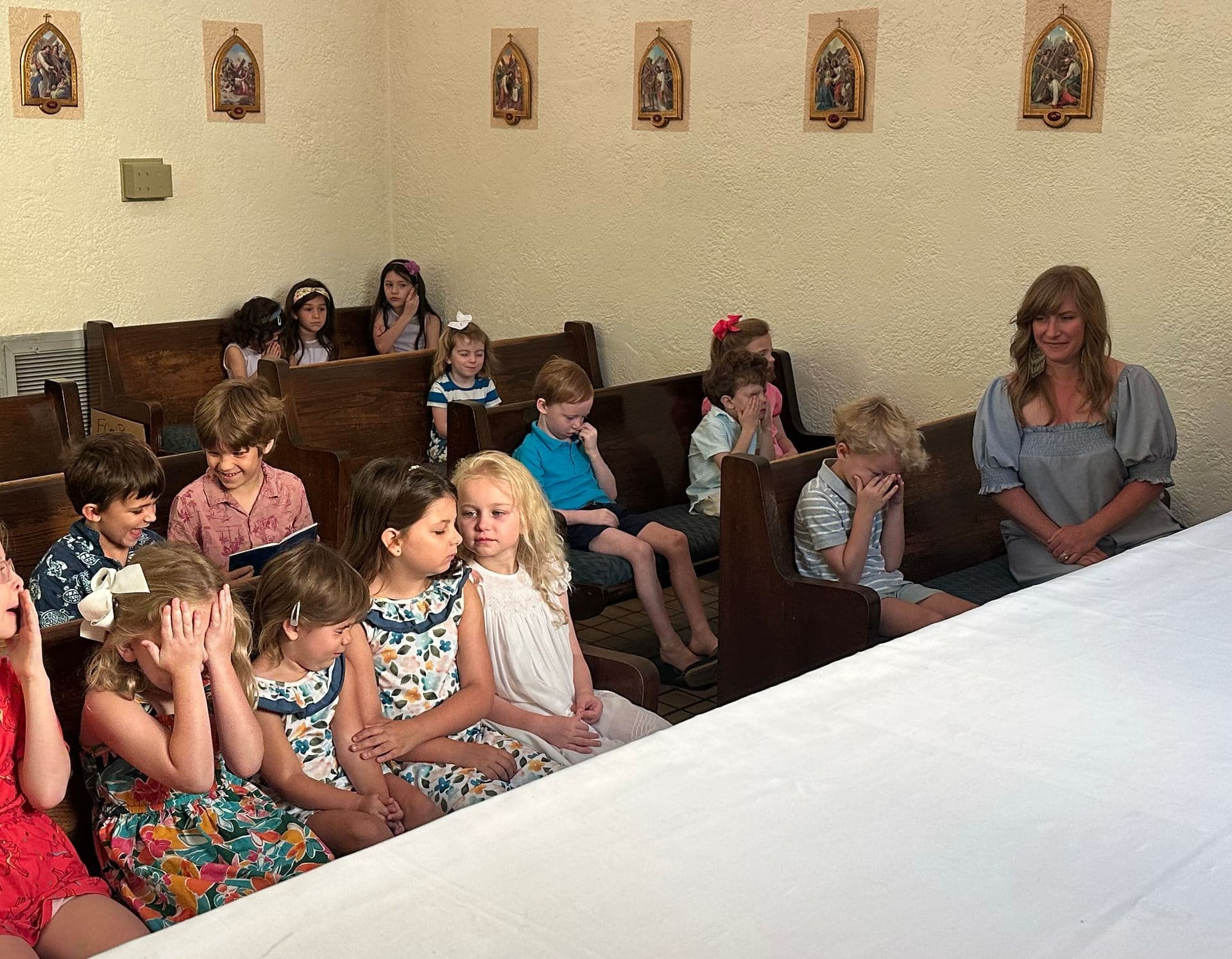 Young students from St. Mary's School seated in the church pews during a school Mass, with framed Stations of the Cross on the wall behind them.